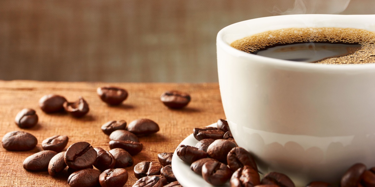 A close up photo of a cup of coffee and scattered coffee beans on top of a cloth-covered surface
