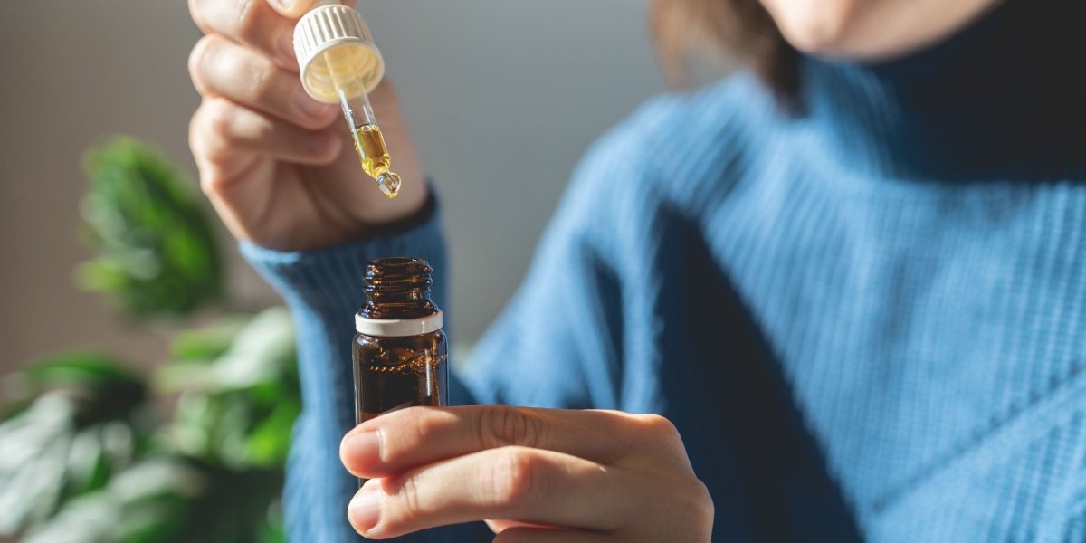 A close up photo of a woman in blue sweatshirt as she's holding a small bottle of THC and a dropper