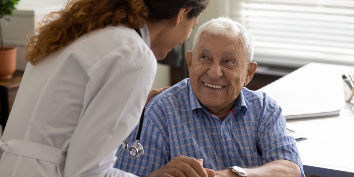 A close up photo of an elderly patient in recovery smiling at a healthcare worker