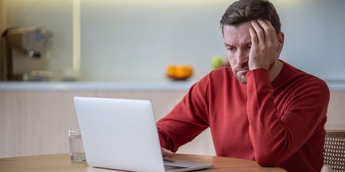 A photo of a Caucasian man in front of his laptop but is unable to concentrate and feeling irritable due to aripiprazole withdrawal