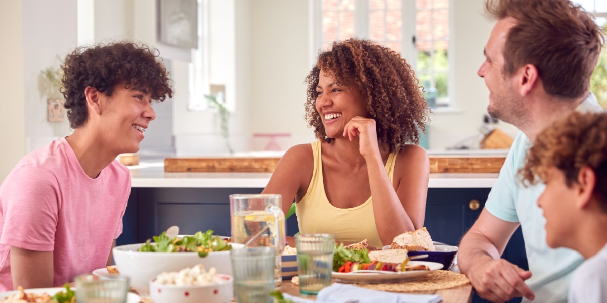 A photo of a family of four sitting together at the table for a meal and having a good conversation with their teenage son.