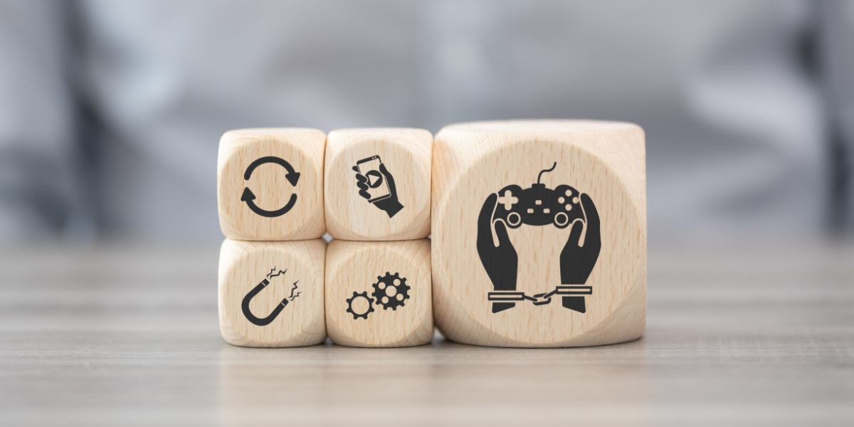 A close up photo of wooden blocks on top of a table. The wooden blocks have icons that symbolize video gaming and social media addiction.