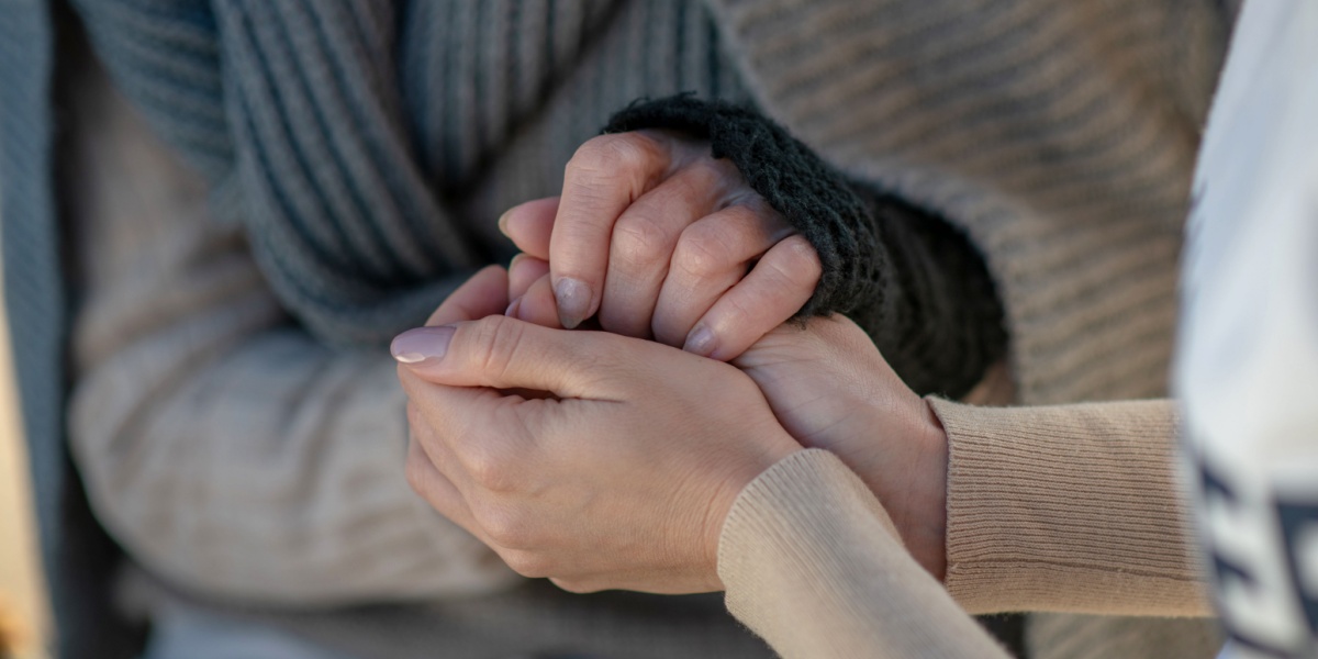 A close up photo of a volunteer holding the hands of a homeless woman closely and warmly