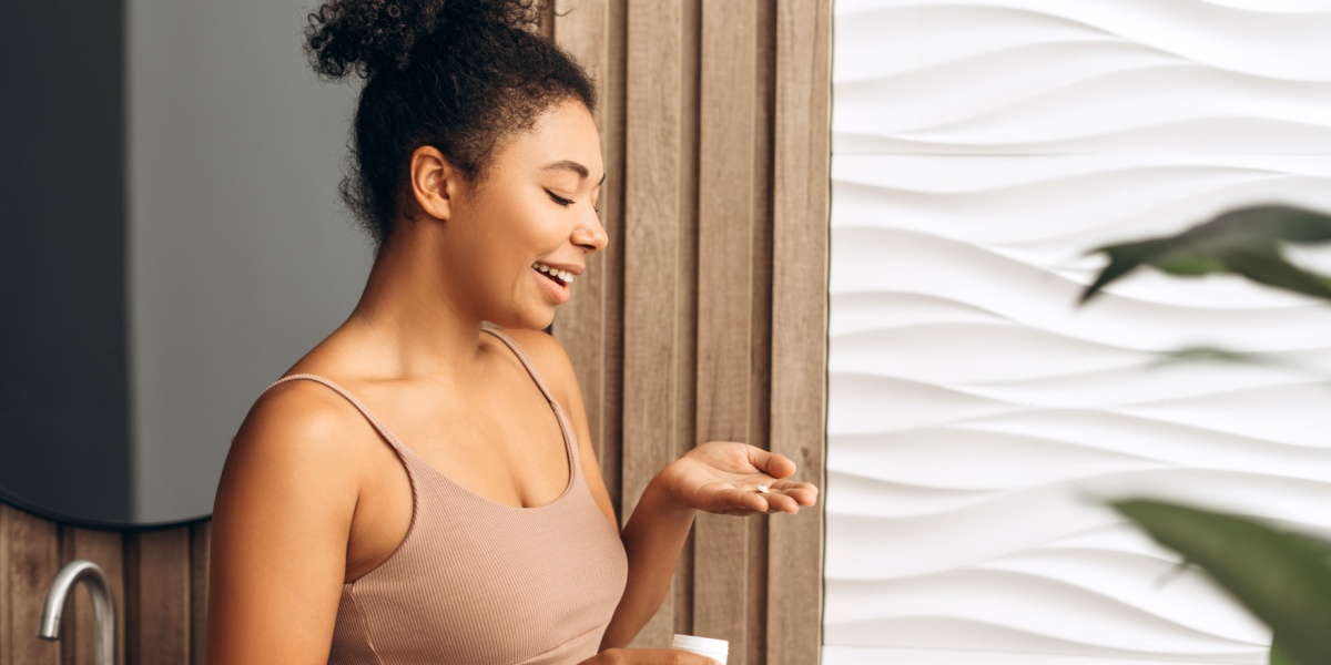 A photo of a Black woman in a bathroom holding a Lomotil pill in her hand