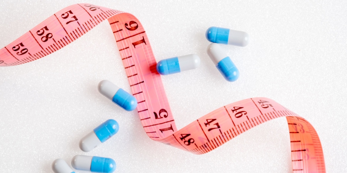A photo of Cymbalta pills lined in a haphazard diagonal line and a pink measuring tape running perpendicular to it