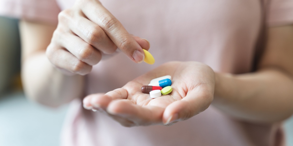 A close up photo of a hand holding a methocarbamol pill along with other pills and capsules.