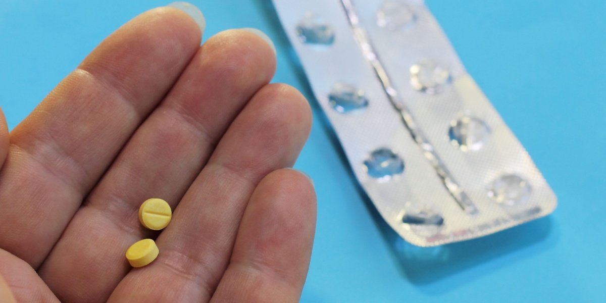 A close up photo of a hand holding Flualprazolam pills, as if about to consume, and a Flualprazolam blister pack on the side.
