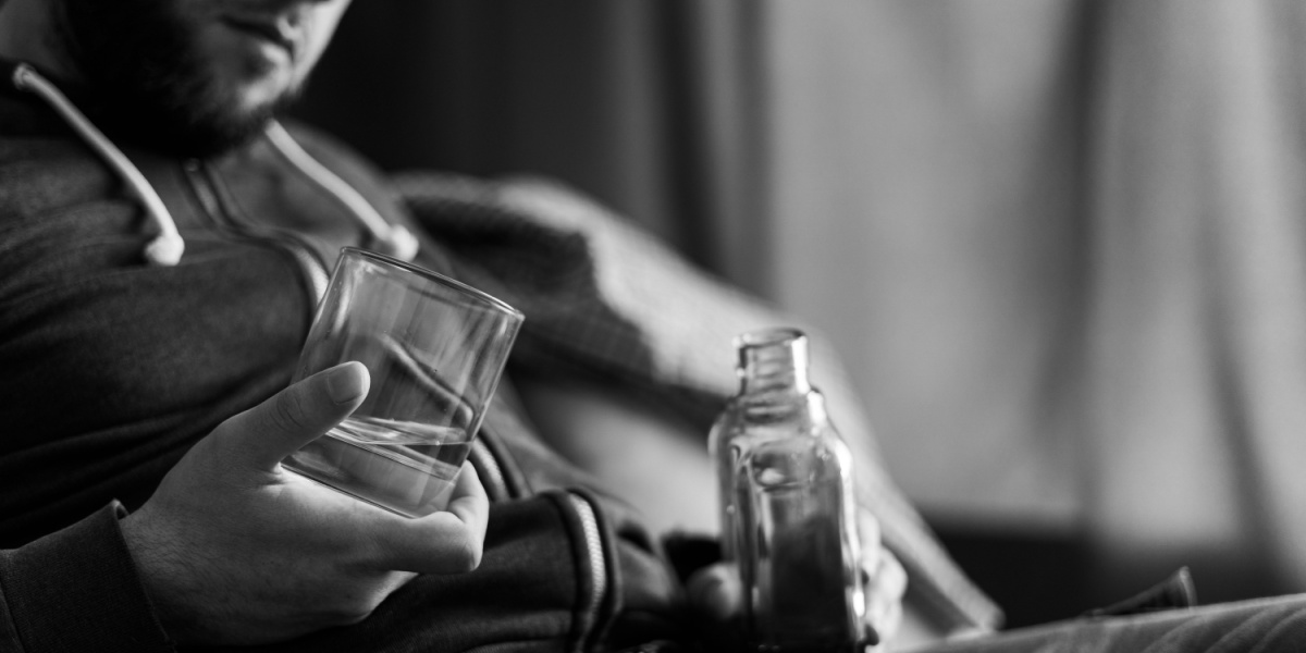A grey-colored photo of a man holding a glass and an alcohol bottle.