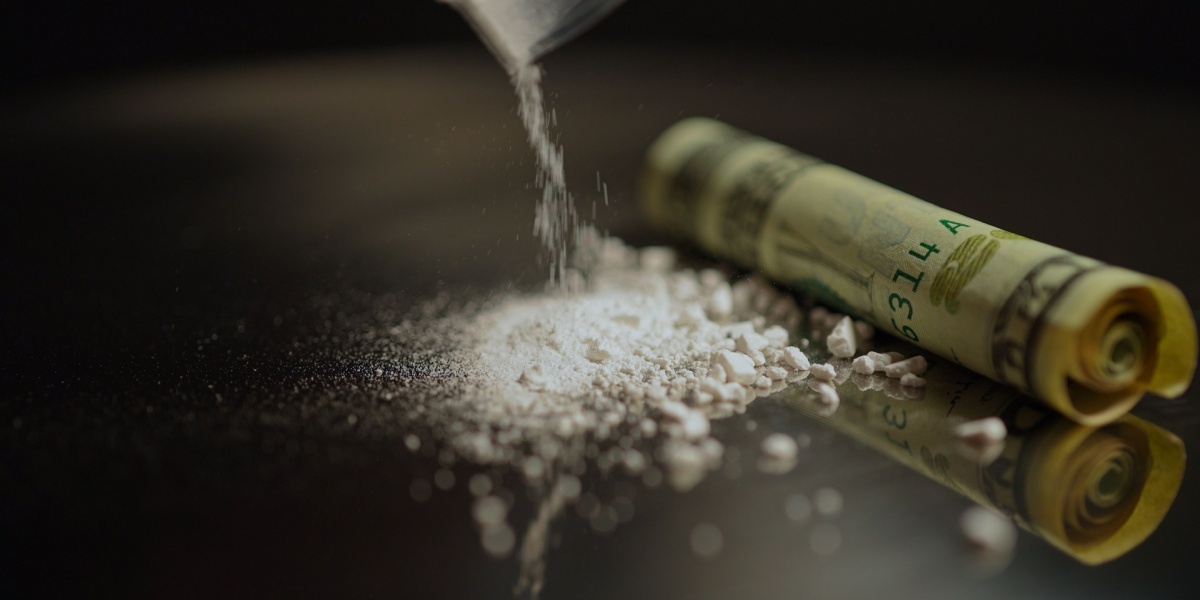A close up of cocaine powder being poured from a plastic container on to a dark table.